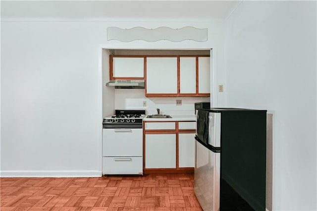 kitchen with under cabinet range hood, a sink, white gas range oven, white cabinetry, and freestanding refrigerator