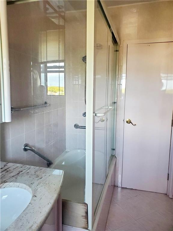 bathroom featuring tile patterned floors, vanity, enclosed tub / shower combo, and tile walls