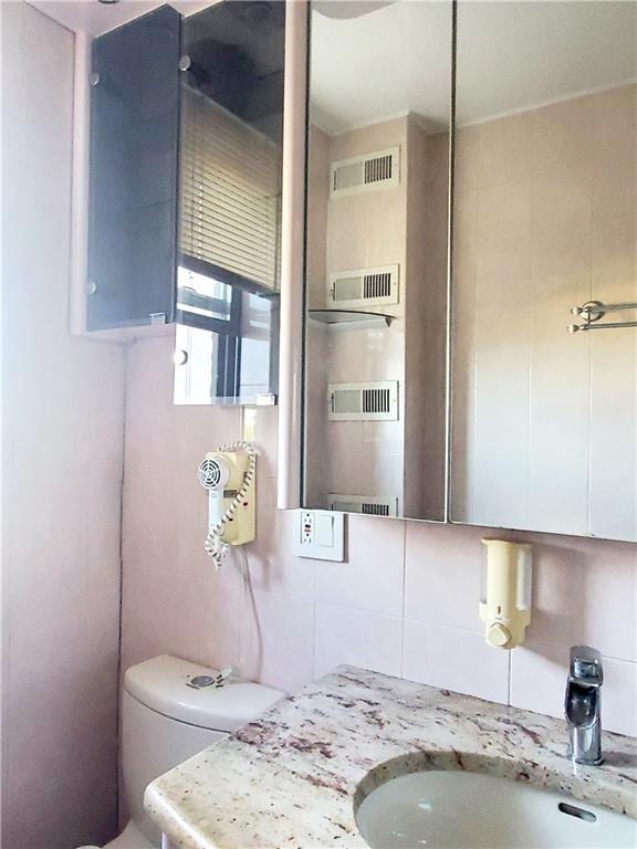 bathroom with vanity, toilet, decorative backsplash, and tile walls