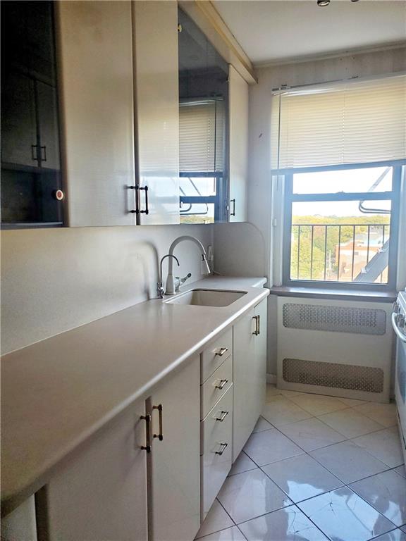 kitchen with a sink, radiator, light countertops, and white cabinetry