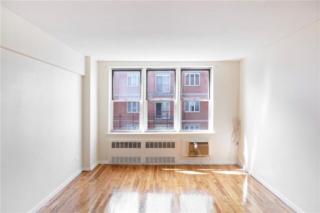 empty room with radiator, light hardwood / wood-style floors, and a wall unit AC