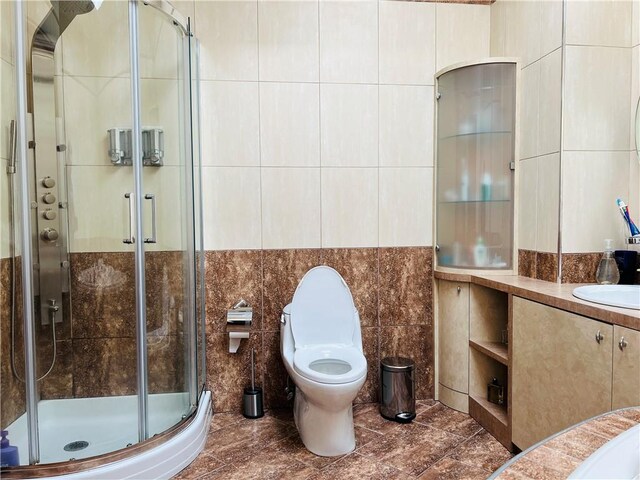 bathroom featuring vanity, a shower with shower door, tile walls, and toilet