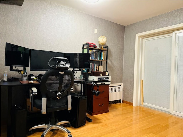 office with radiator heating unit and light hardwood / wood-style flooring