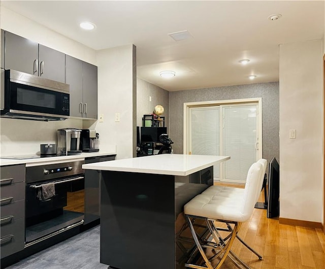 kitchen featuring a kitchen island, a breakfast bar, gray cabinetry, light hardwood / wood-style floors, and black appliances