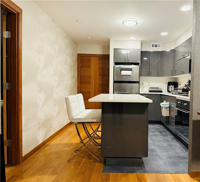 kitchen with a breakfast bar, gray cabinets, a center island, and oven