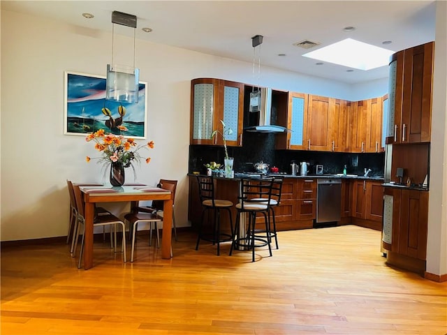 kitchen with decorative backsplash, dark countertops, wall chimney exhaust hood, light wood-style flooring, and decorative light fixtures