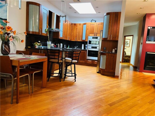 kitchen with double oven, a skylight, ventilation hood, decorative light fixtures, and light hardwood / wood-style floors