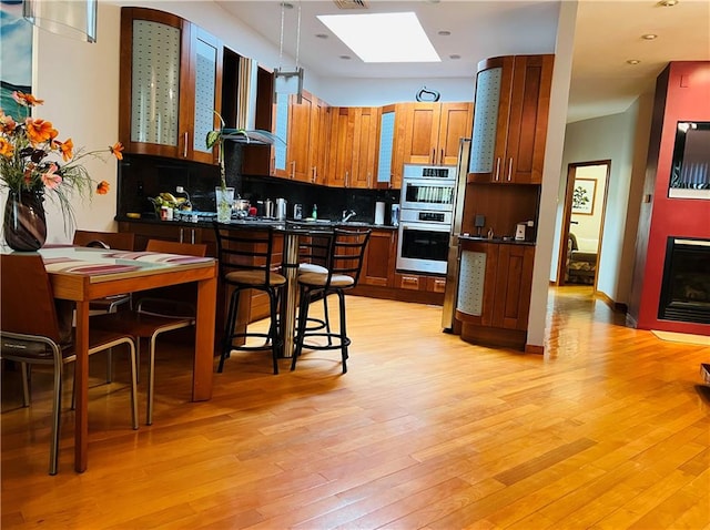 kitchen featuring wall chimney exhaust hood, stainless steel double oven, dark countertops, and light wood-style floors