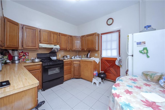 kitchen with decorative backsplash, light tile patterned flooring, black range with gas cooktop, and white refrigerator