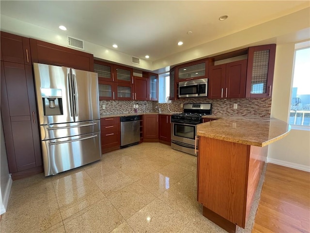 kitchen with light stone countertops, stainless steel appliances, backsplash, and kitchen peninsula