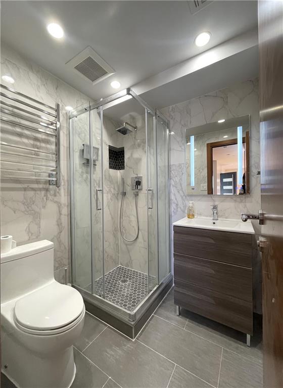 bathroom with vanity, tile walls, toilet, and a shower with door