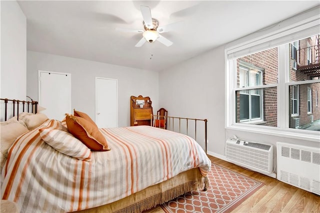 bedroom featuring ceiling fan, light wood-type flooring, radiator heating unit, and a wall mounted AC