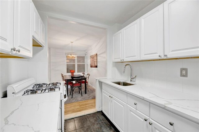 kitchen with light stone counters, a sink, white cabinets, white gas range oven, and pendant lighting