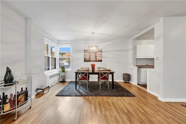 dining space with radiator heating unit, an inviting chandelier, and light wood-type flooring