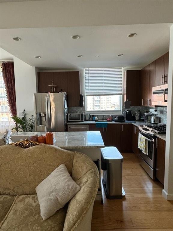 kitchen with appliances with stainless steel finishes, dark brown cabinets, tasteful backsplash, light hardwood / wood-style floors, and a kitchen island