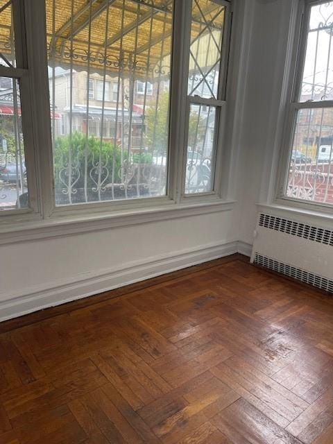 unfurnished dining area with plenty of natural light, radiator heating unit, and dark parquet flooring