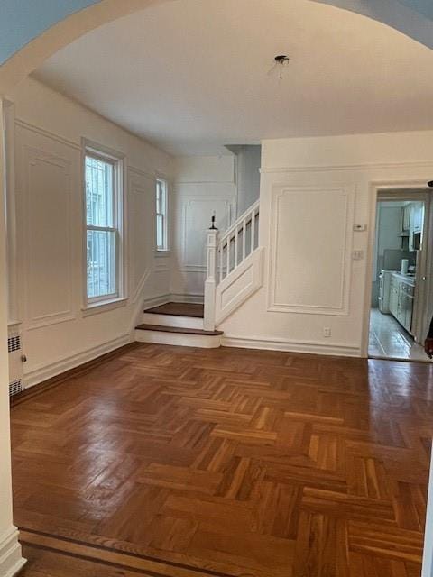 entrance foyer with arched walkways, a decorative wall, stairway, and radiator heating unit