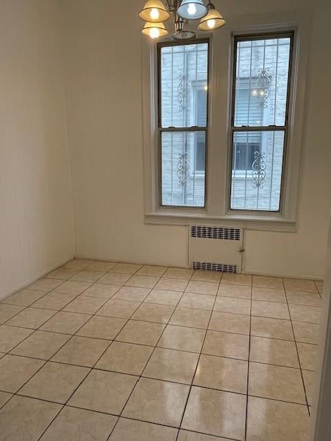 unfurnished room featuring light tile patterned floors, radiator heating unit, and an inviting chandelier