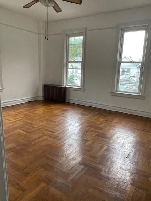 empty room featuring a ceiling fan, baseboards, and radiator heating unit