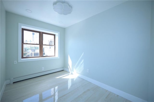 empty room featuring a baseboard heating unit, baseboards, and wood finished floors