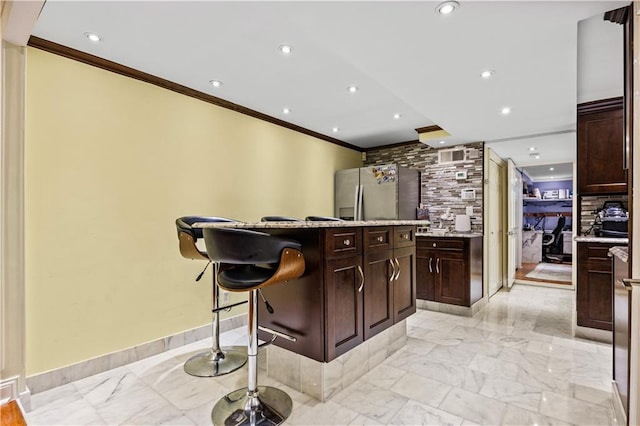 kitchen with backsplash, ornamental molding, light stone countertops, stainless steel fridge with ice dispenser, and a kitchen bar