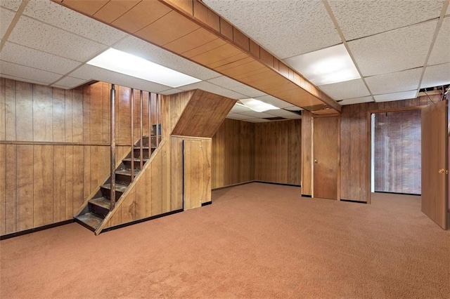 finished basement with carpet, wooden walls, and stairs