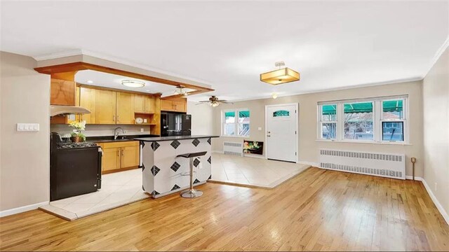 kitchen featuring black appliances, ceiling fan, light wood-type flooring, light brown cabinetry, and radiator heating unit