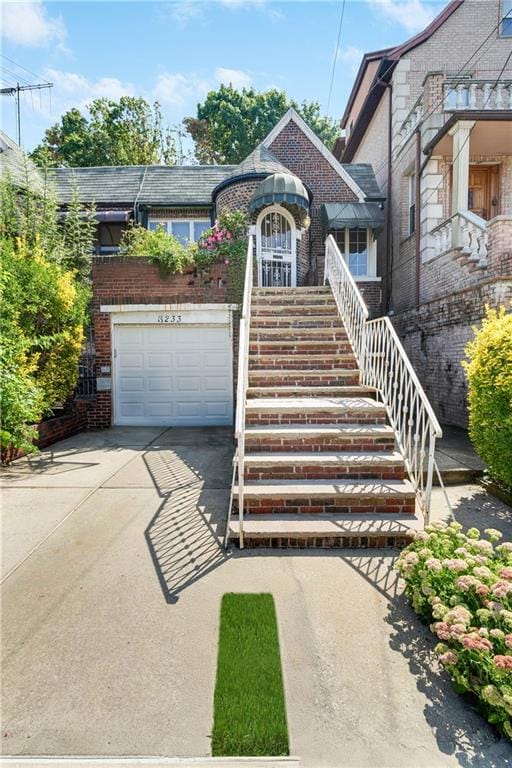 view of front of property with brick siding, driveway, an attached garage, and stairs