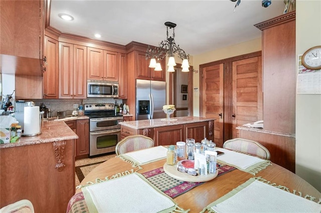 kitchen with light stone countertops, appliances with stainless steel finishes, an inviting chandelier, a center island, and hanging light fixtures