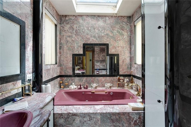 bathroom featuring tiled bath, vanity, a skylight, and tile walls