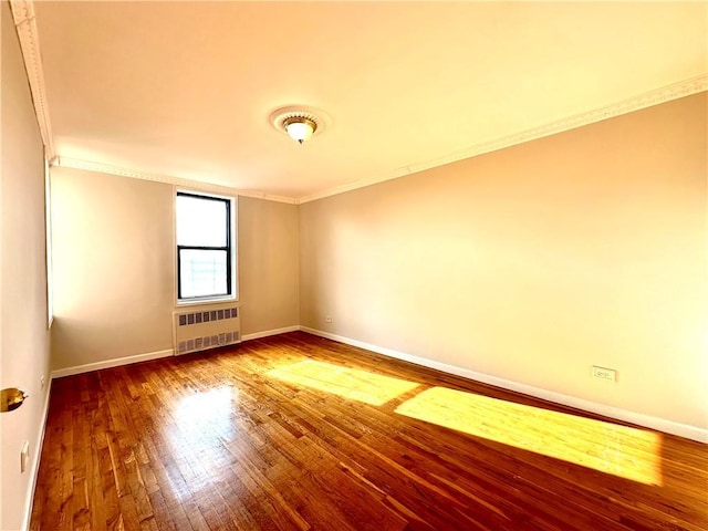 unfurnished room featuring baseboards, crown molding, radiator heating unit, and wood finished floors