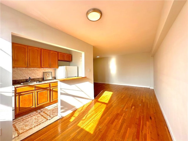 kitchen featuring white refrigerator, sink, light hardwood / wood-style floors, and decorative backsplash