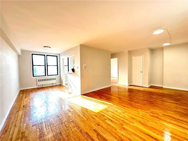 spare room with baseboards, radiator heating unit, and wood finished floors