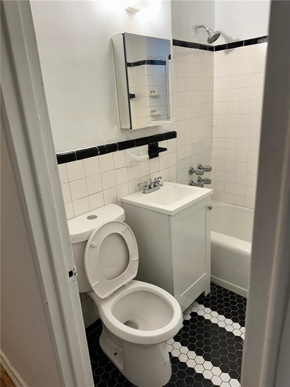 bathroom featuring tile walls, toilet, tile patterned floors, vanity, and  shower combination