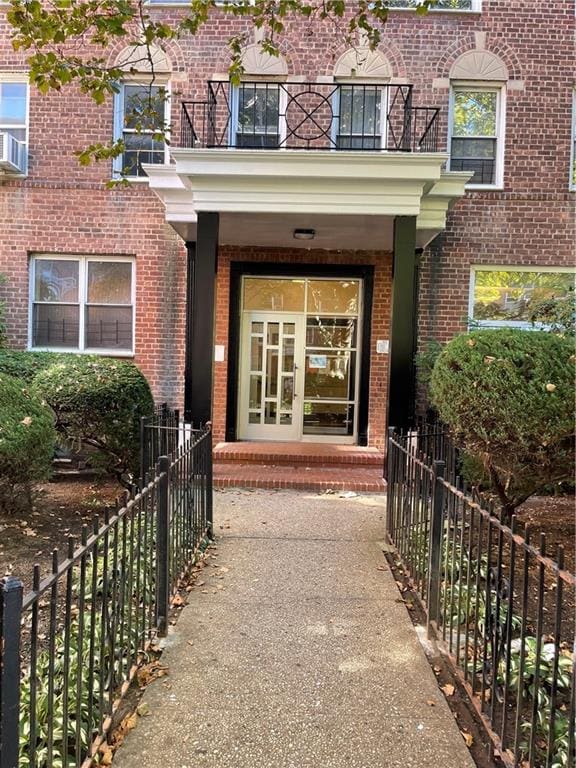 view of exterior entry with brick siding, a balcony, and fence