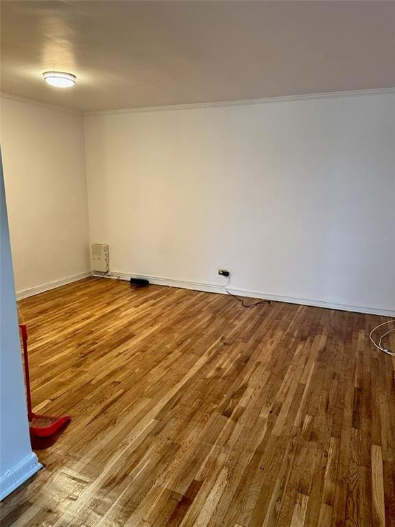 empty room featuring crown molding, baseboards, and wood finished floors