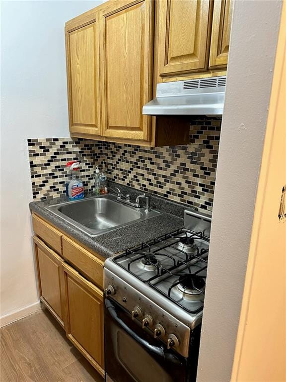 kitchen with dark countertops, under cabinet range hood, a sink, gas range, and backsplash