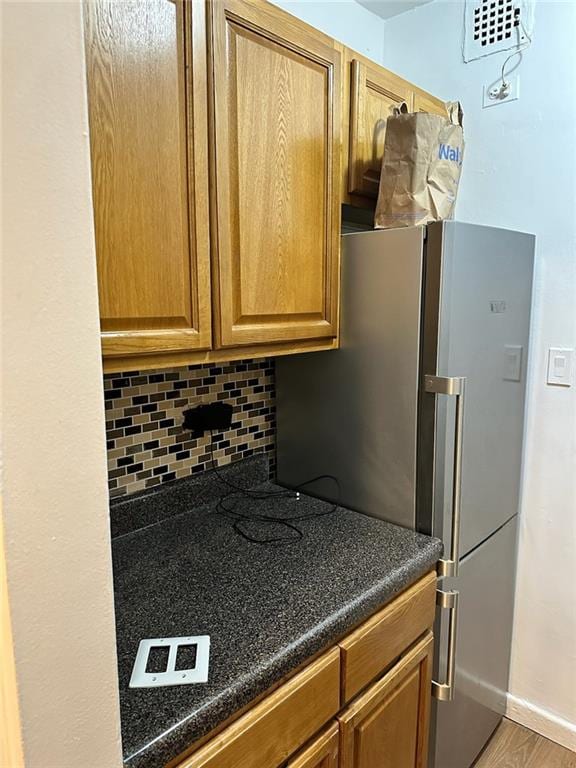 kitchen with tasteful backsplash, baseboards, dark countertops, freestanding refrigerator, and brown cabinets