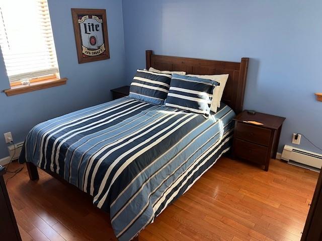 bedroom with a baseboard radiator, baseboards, and wood finished floors