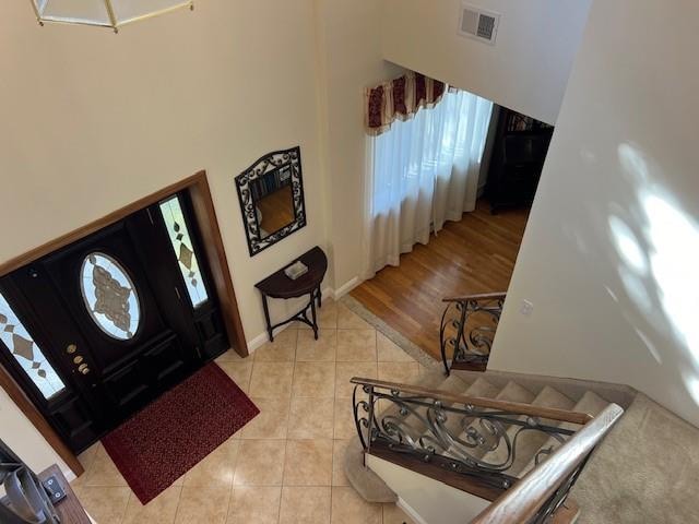 foyer with light tile patterned floors, visible vents, baseboards, and a high ceiling