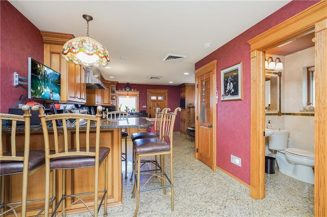 kitchen with wall chimney exhaust hood, kitchen peninsula, and a breakfast bar area