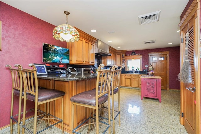 kitchen with a breakfast bar area, kitchen peninsula, hanging light fixtures, and wall chimney range hood