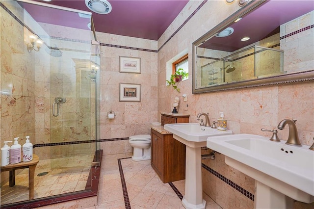 bathroom with tile patterned floors, walk in shower, dual sinks, tile walls, and toilet