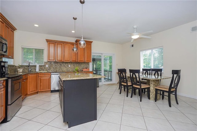 kitchen featuring appliances with stainless steel finishes, light stone counters, ceiling fan, a kitchen island, and hanging light fixtures