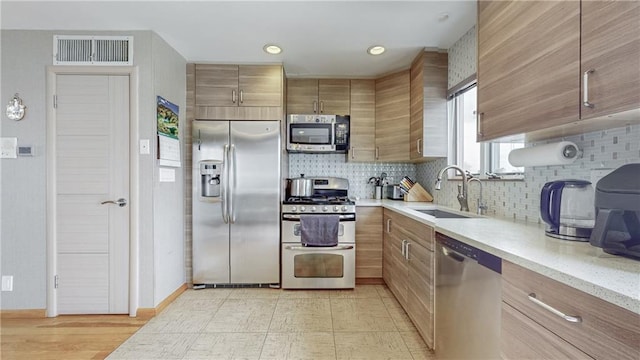 kitchen with brown cabinets, visible vents, decorative backsplash, appliances with stainless steel finishes, and a sink