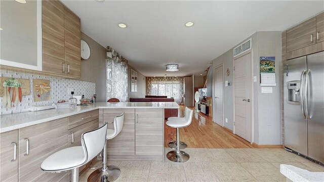 kitchen featuring backsplash, a kitchen breakfast bar, kitchen peninsula, and built in refrigerator