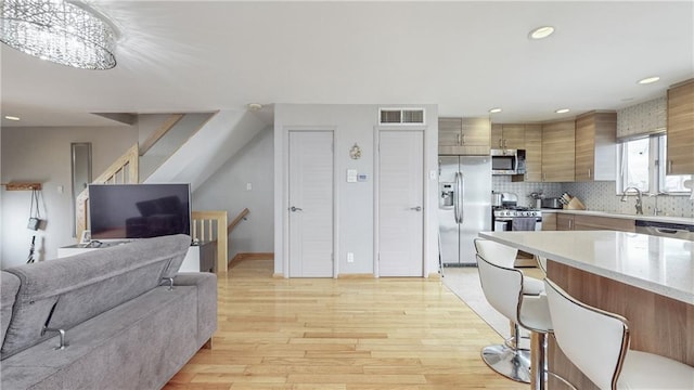 kitchen with light countertops, visible vents, appliances with stainless steel finishes, light wood-type flooring, and a kitchen bar