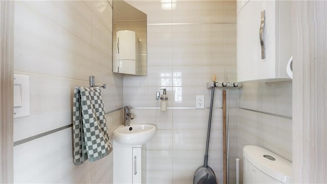 bathroom with toilet, a sink, and tile walls