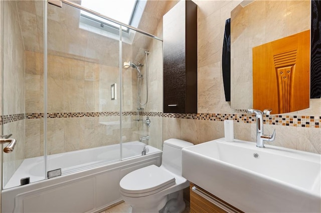 full bathroom with bath / shower combo with glass door, vanity, tile walls, and toilet