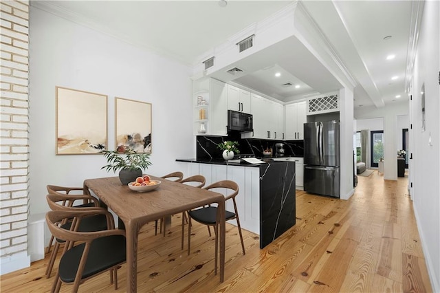 kitchen with visible vents, backsplash, black microwave, light wood-type flooring, and freestanding refrigerator